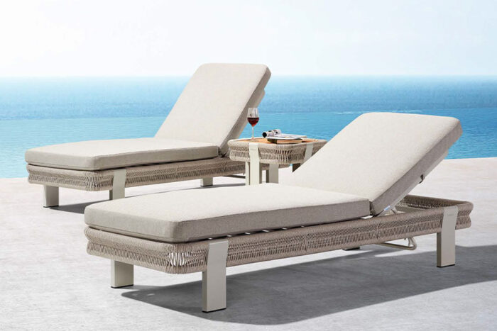 Deux bains de soleil haut de gamme en poly rotin beige, résine tressée à la main. Table d'appoint supportant des boissons. Collection Borromeo
