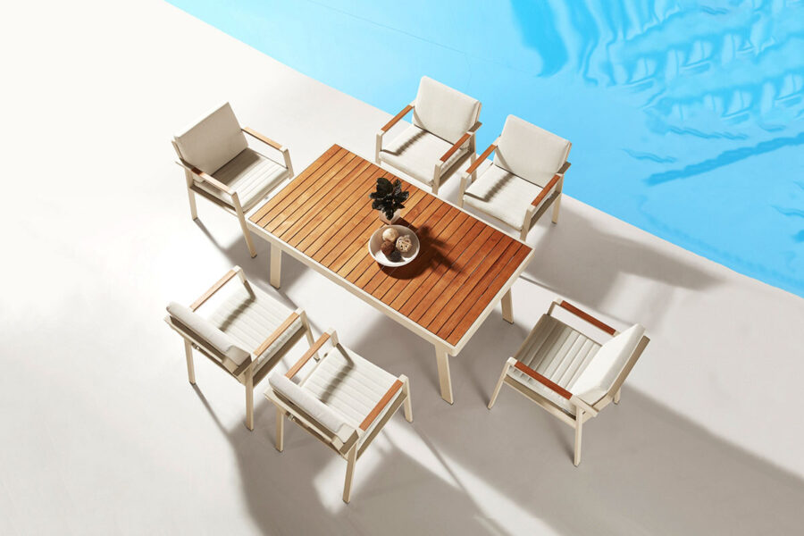 Ensemble table et chaises de jardin blanches haut de gamme 6 personnes Nofi. Plateau en teck massif, l'aluminium écru, tissu beige. Situé sur une terrasse au bord d'une piscine.