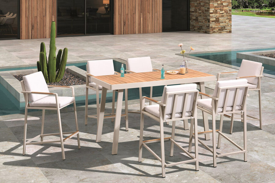 Ensemble table haute de bar et 6 chaises haut de gamme en alu blanc et teck Nofi. Présenté sur une belle terrasse avec bassins et cactus.